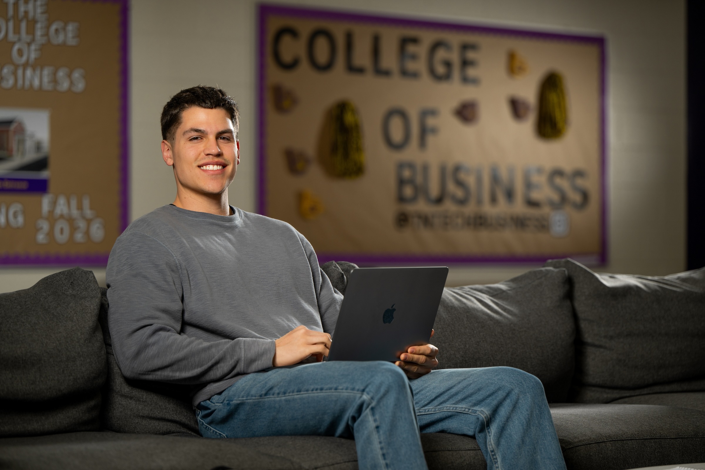 Westley Hunter seated on a couch holding an open laptop, smiling at the camera